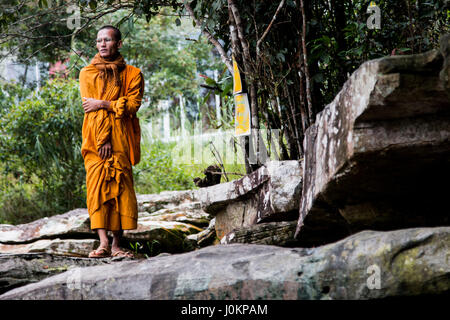 Un monaco guardando fuori ad una cascata in un parco nazionale in Cambogia Foto Stock