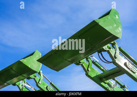 Parte della moderna verde macchine escavatore,le benne-pale sollevate contro il cielo blu in un sito in costruzione. Foto Stock