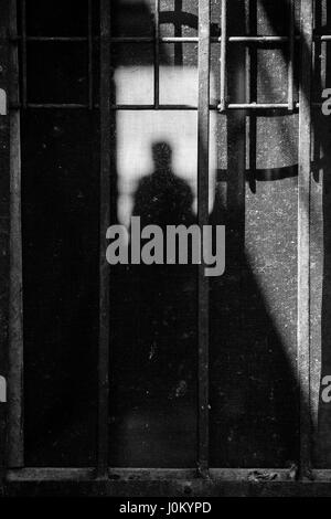 Stagliano uomo in ombre attraverso un schermo arrugginita porta. Foto Stock