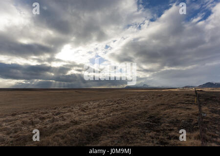 Raggi di sole rompere attraverso le nuvole, colpendo i campi dorati nella valle sottostante. Snaefellsnes (Snaefellsnes) penisola, western Islanda Foto Stock