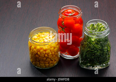 Tre vasi aperti con granturco dolce, pomodorini e broccoli sul bordo scuro. Copia spazio sulla sinistra. Foto Stock