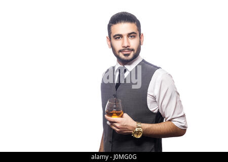 Bello barbuto imprenditore tenendo un bicchiere di whiskey. tenendo il vetro, sorridente e guardando la fotocamera. studio shot, isolato su sfondo bianco. Foto Stock