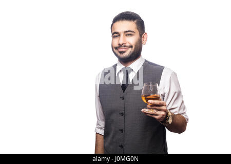 Bello barbuto imprenditore tenendo un bicchiere di whiskey. Sorridendo e guardando la fotocamera. studio shot, isolato su sfondo bianco. Foto Stock