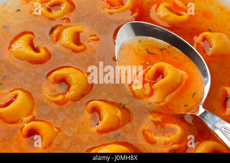 Recentemente bollita e tortellini in recipiente di vetro con brodo piccante. Tortellini unico sul cucchiaio. Full frame foto. Foto Stock