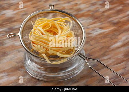 Pasta grezza di pasta in cucina in metallo su setaccio dipinta sullo sfondo di materie tessili Foto Stock