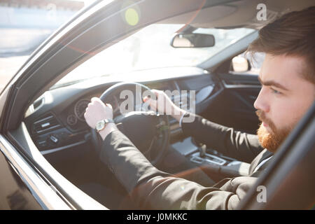 Immagine ritagliata di uomo barbuto in tuta la guida auto e guardando lontano Foto Stock