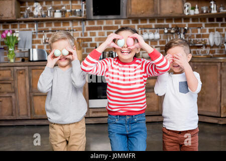 Tre graziosi ridere i bambini a giocare con le uova di pasqua in cucina Foto Stock