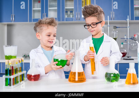 Poco sorridenti ragazzi in camice da laboratorio rendendo esperimento in laboratorio chimico Foto Stock