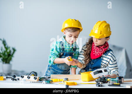 Piccolo Ragazzo e ragazza di copricapi rigidi suonare con strumenti giocattolo in officina Foto Stock