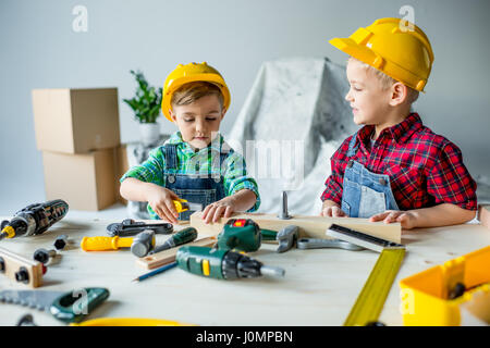 Simpatici ragazzi piccoli nel duro cappelli suonare con strumenti giocattolo in officina Foto Stock