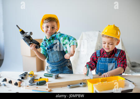 Due poco sorridenti ragazzi nel duro cappelli suonare con strumenti giocattolo in officina Foto Stock