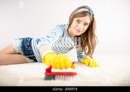 Giovane donna in giallo guanti in gomma Tappeto di pulizia con spazzola Foto Stock