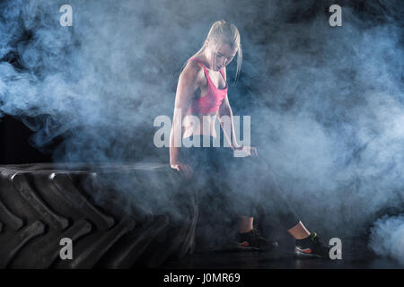 Vista laterale della donna in abbigliamento sportivo seduto sul pneumatico Foto Stock