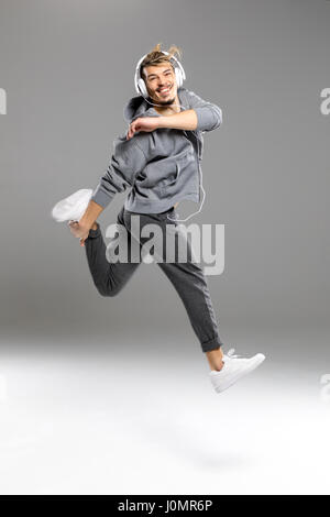 Atletica Giovane uomo nelle cuffie jumping mentre sorridente in telecamera Foto Stock