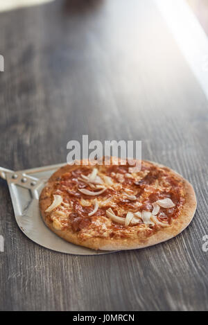 Appena cotto alla griglia di fiamma pizza italiana su una crosta croccante su un contatore di legno in una pizzeria con copia spazio sopra Foto Stock