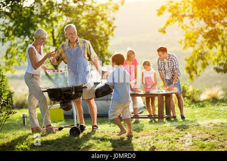 Nipote nonni aiuta a fare un barbecue per la famiglia Foto Stock