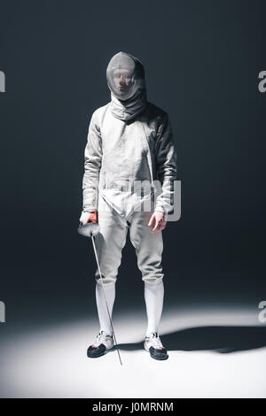 Professional fencer nella scherma con maschera di rapier in piedi su grigio Foto Stock