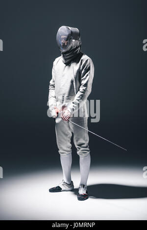 Professional fencer nella scherma con maschera di rapier in piedi su grigio Foto Stock