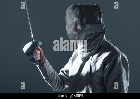 Ritratto di professional fencer nella scherma con maschera di rapier su grigio Foto Stock