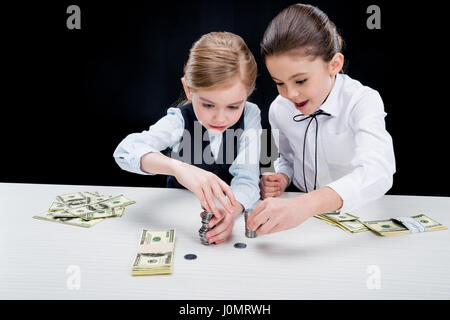 Ritratto di bambine seduti a tavola e il calcolo di denaro su nero Foto Stock