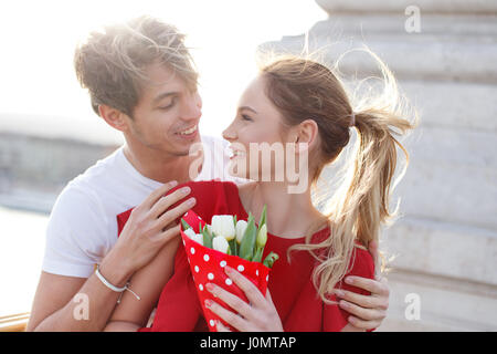 Felice coppia giovane risalente all'aperto, donna in abito rosso e bouquet Foto Stock