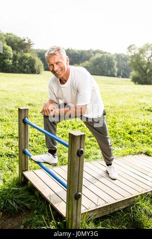 Senior uomo appoggiata sul gate, sorridente. Foto Stock