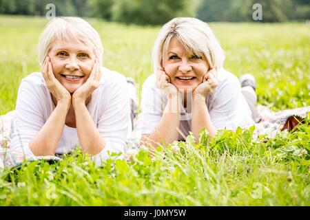 Due donne che giace sull'erba con le mani sul mento. Foto Stock