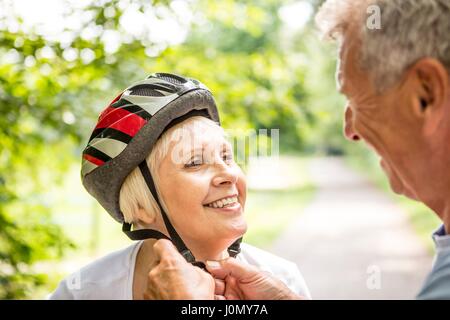 Donna matura che indossa il casco per bicicletta, senior uomo assistere. Foto Stock