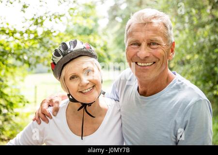 Donna matura che indossa il casco per bicicletta, senior uomo con braccio intorno a lei. Foto Stock