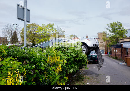 Wallington, Surrey, Regno Unito. Il 15 aprile, 2017. Una vettura si è schiantato attraverso una siepe in Shotfied parcheggio in Wallington, Surrey. L'estremità anteriore si blocca procariously su una strada di servizio nella parte posteriore di negozi. Non è chiaro se la vettura ha perso il controllo o è stata deliberatamente si è schiantato che sono stati rubati. Forze di polizia sono presenti. Sabato 15 Aprile 2017. Wallington, London Borough of Sutton. Credito: Darren Lehane/Alamy Live News Foto Stock