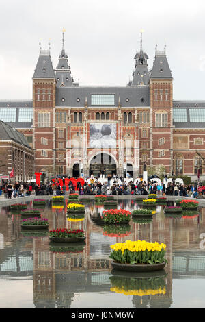 La facciata del Rijksmuseum con la Iamsterdam segno e il lago con tulipani galleggianti di fronte ad esso. Foto Stock