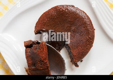 Gu cioccolata calda partecentrale fuso budini - cucchiaio che mostra l'interno, sempre pronto a mangiare Gu cioccolato caldo fuso budino partecentrale sulla piastra bianca Foto Stock