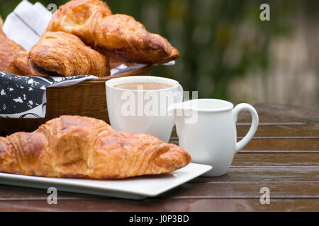 Croissant, una tazza di caffè e latte, su di un tavolo di legno nella luce naturale. Foto Stock