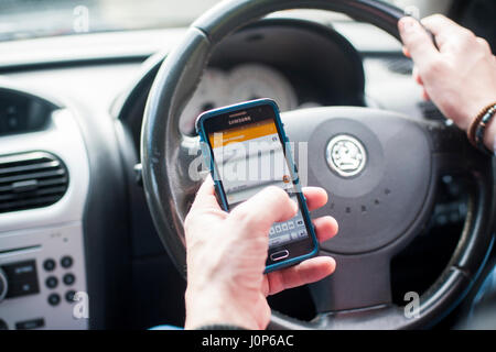 Uomo che utilizza il telefono cellulare sms durante la guida Foto Stock