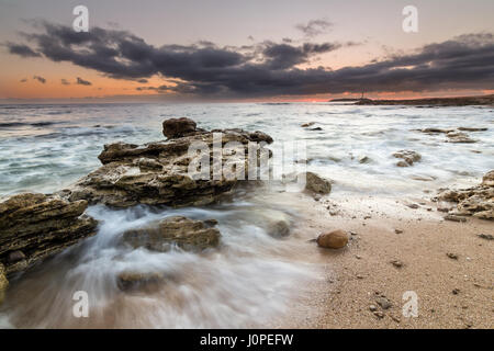 Tramonto con le onde che si infrangono sulle rocce e il faro di Trafalgar in background, Cadice, Andalusia, Spagna Foto Stock