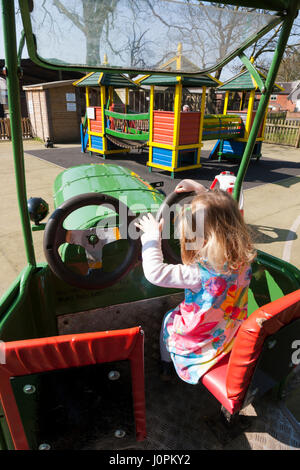 Due ragazze riprodotto nell'area di gioco con una riproduzione di un modello in scala del trattore a Glebe Farm, Astbury, Congleton, Cheshire. Regno Unito. (87) Foto Stock