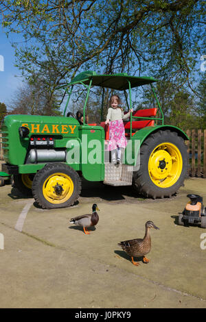 Due ragazze riprodotto nell'area di gioco con una riproduzione di un modello in scala del trattore a Glebe Farm, Astbury, Congleton, Cheshire. Regno Unito. (87) Foto Stock