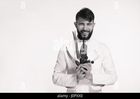 Studio shot di una felice barbuto giovane chef azienda coltelli affilati su sfondo bianco. Chef con il coltello. Bello sorridente ridere cheef tenendo molti sh Foto Stock