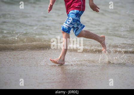 Fistral Newquay persona che corre lungo il litorale Splash Splashing Runner Spray Acqua Barefoot energia energetica Mare Turismo Beach Vacanza Foto Stock