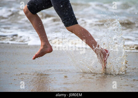 Fistral Newquay persona che corre lungo il litorale Splash Splashing Runner Spray Acqua Barefoot energia energetica Mare Turismo Beach Vacanza Foto Stock