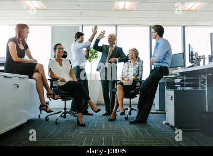 Due allegro la gente di affari dando ad alta cinque mentre i loro colleghi a guardarli e sorridente. Il team di Business godendo il successo in ufficio Foto Stock