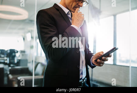 Ritagliato shot di imprenditore tramite cellulare in ufficio e pensare. Maschio azienda executive smart phone. Foto Stock