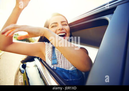 Donna seduta in onde di auto le braccia e ride come lei si affaccia alla finestra Foto Stock