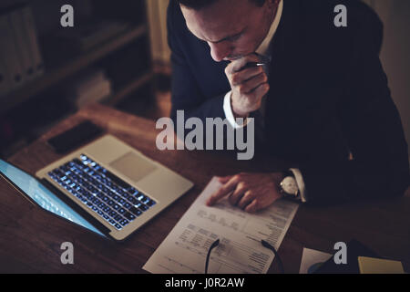 Imprenditore pensieroso seduto in ufficio e facendo la documentazione di notte. Foto Stock