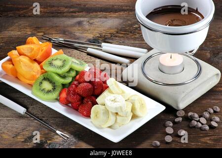 La Fonduta di cioccolato con frutta assortimento su sfondo di legno Foto Stock