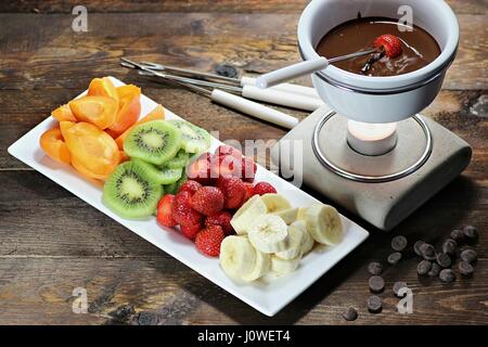 La Fonduta di cioccolato con frutta assortimento su sfondo di legno Foto Stock