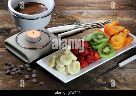 La Fonduta di cioccolato con frutta assortimento su sfondo di legno Foto Stock