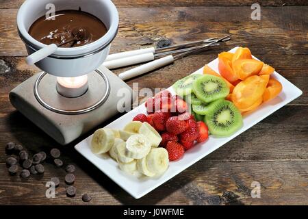 La Fonduta di cioccolato con frutta assortimento su sfondo di legno Foto Stock