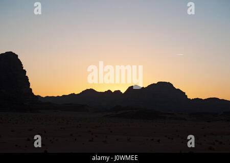 Un tramonto sul contorno scuro di una montagna nel Wadi Rum desert, la famosa Valle della Luna guardando come il pianeta di Marte Foto Stock