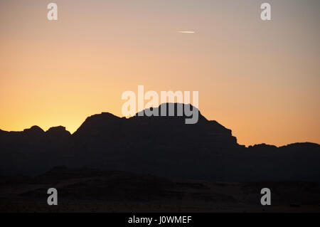 Un tramonto sul contorno scuro di una montagna nel Wadi Rum desert, la famosa Valle della Luna guardando come il pianeta di Marte Foto Stock